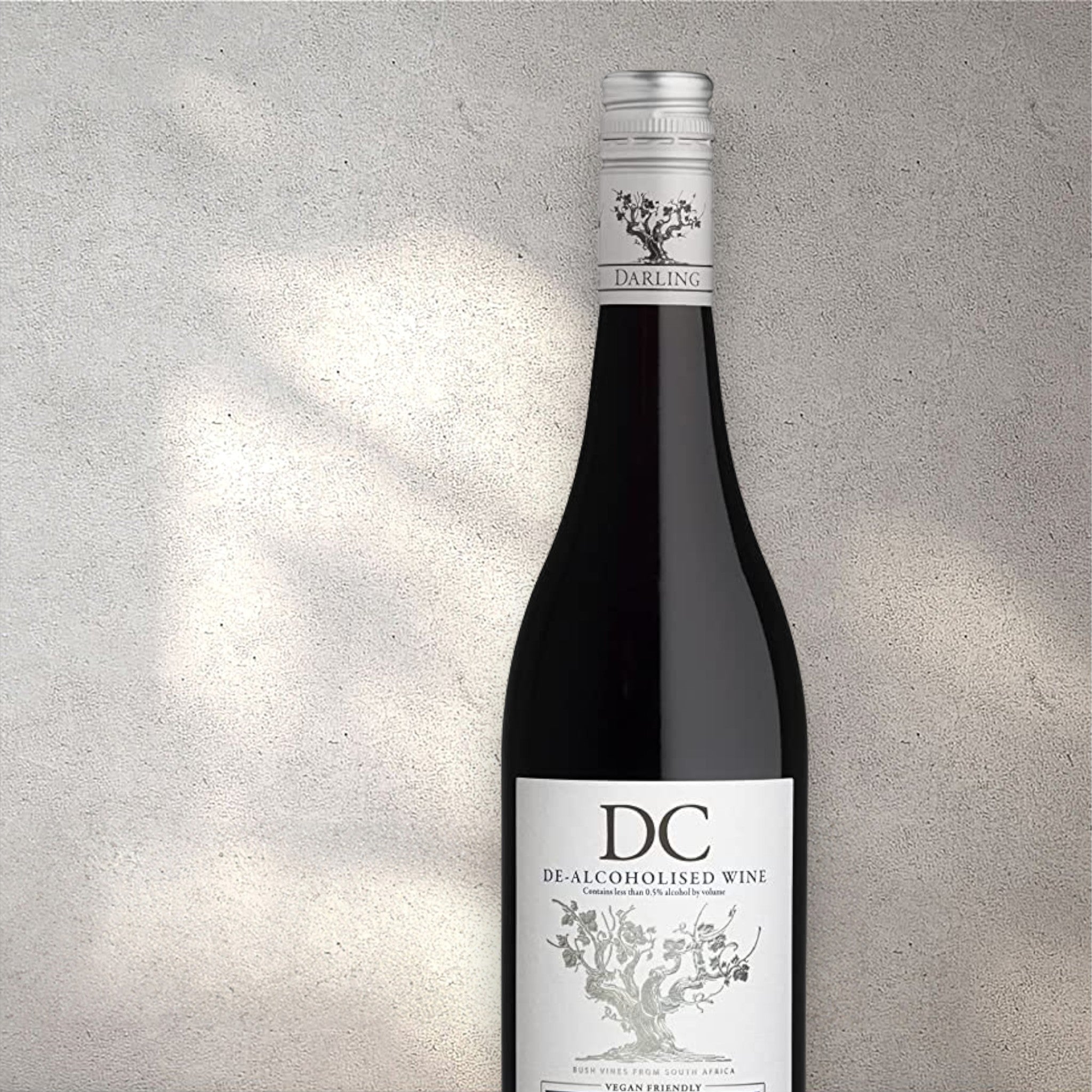 Closeup of a Darling Cellars alcohol-free red wine bottle with a detailed label, set against a textured concrete wall, highlighting its refined design and deep red colour.