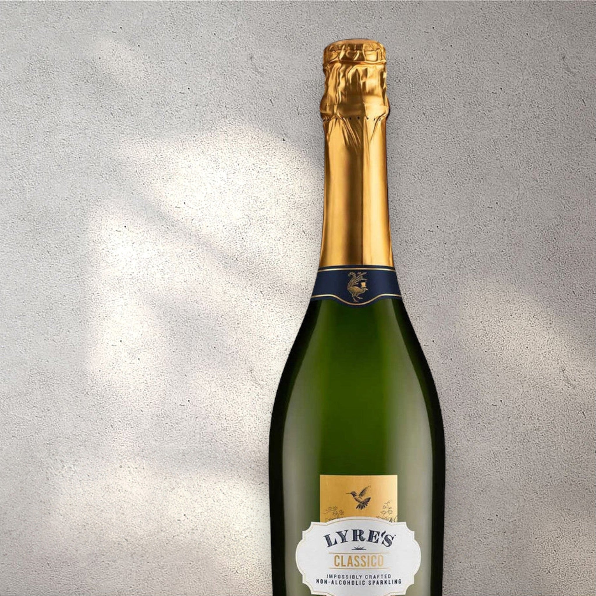 Closeup of a Lyre's Classico alcohol-free sparkling wine bottle with a detailed label, set against a textured concrete wall, highlighting its refined design and clear, sparkling colour.