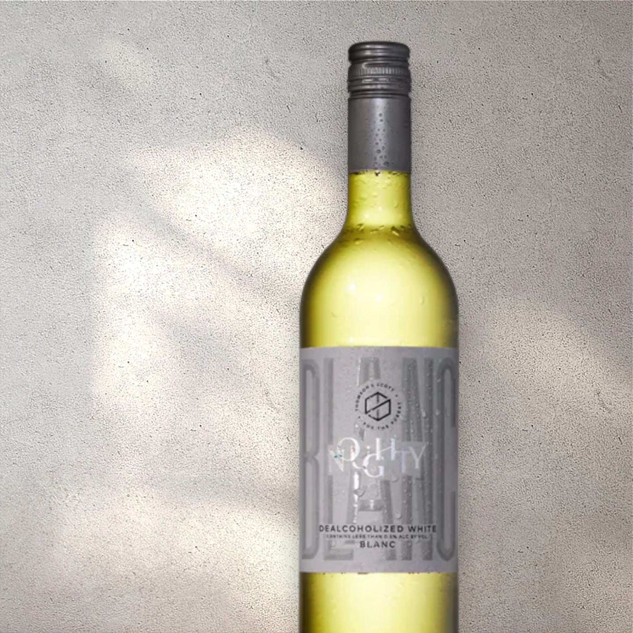Closeup of a Thomson & Scott Noughty alcohol-free white wine bottle with a detailed label, set against a textured concrete wall, highlighting its refined design and light yellow color.