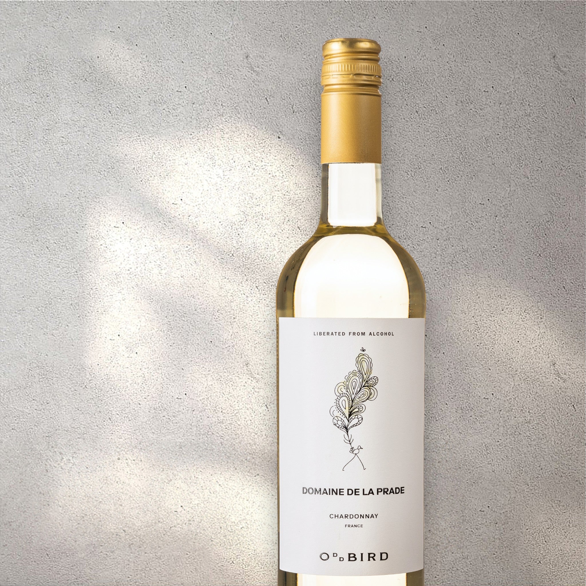 Closeup of an Oddbird Domaine De La Prade alcohol-free white wine bottle with a detailed label, set against a textured concrete wall, highlighting its refined design and light yellow color.