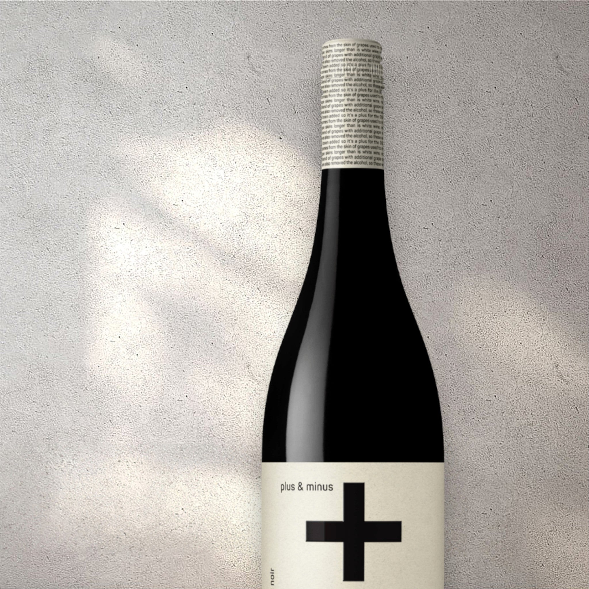 Closeup of a Plus & Minus Pinot Noir alcohol-free red wine bottle with a detailed label, set against a textured concrete wall, highlighting its refined design and deep red color.