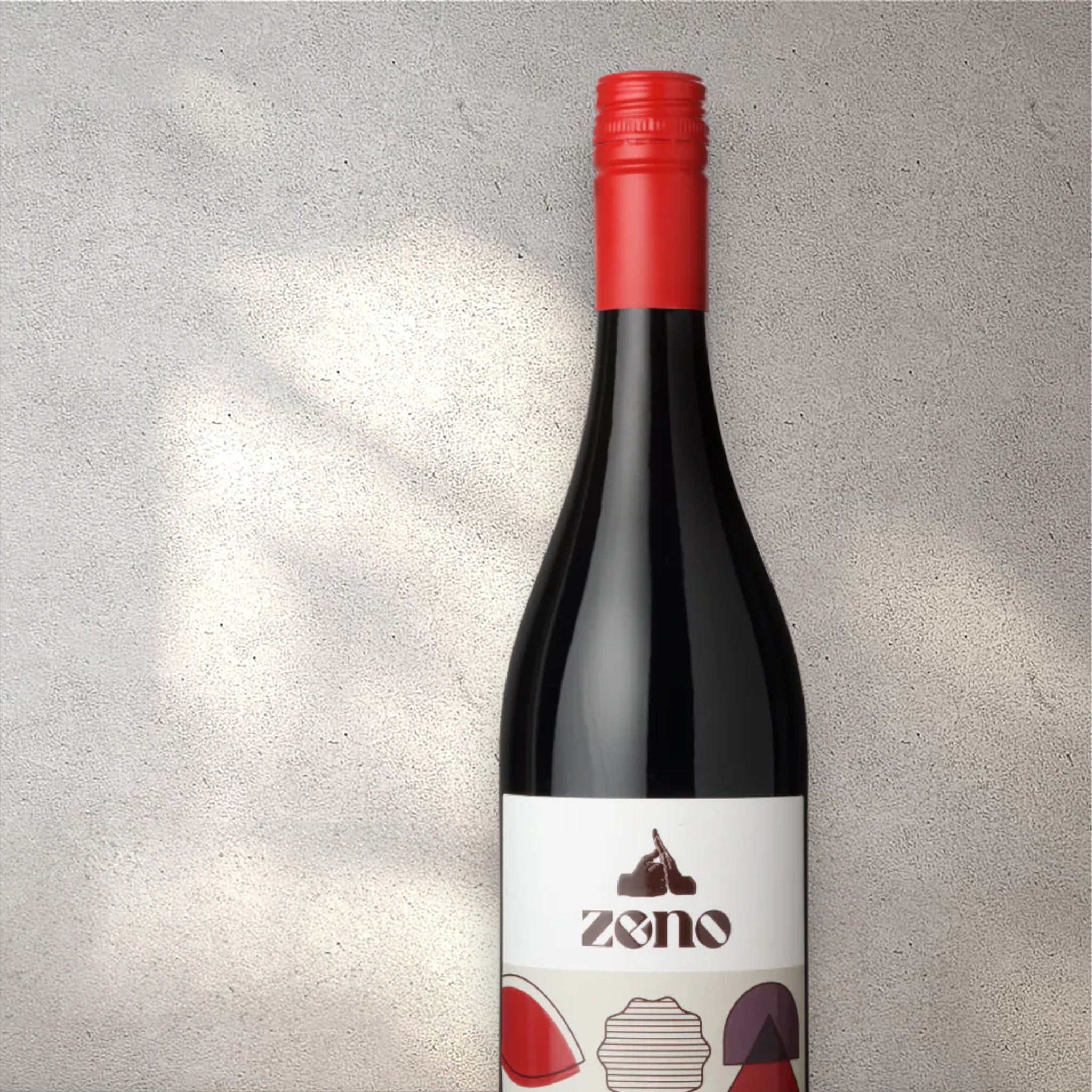 Closeup of a Zeno alcohol-free red wine bottle with a detailed label, set against a textured concrete wall, highlighting its refined design and deep red color.