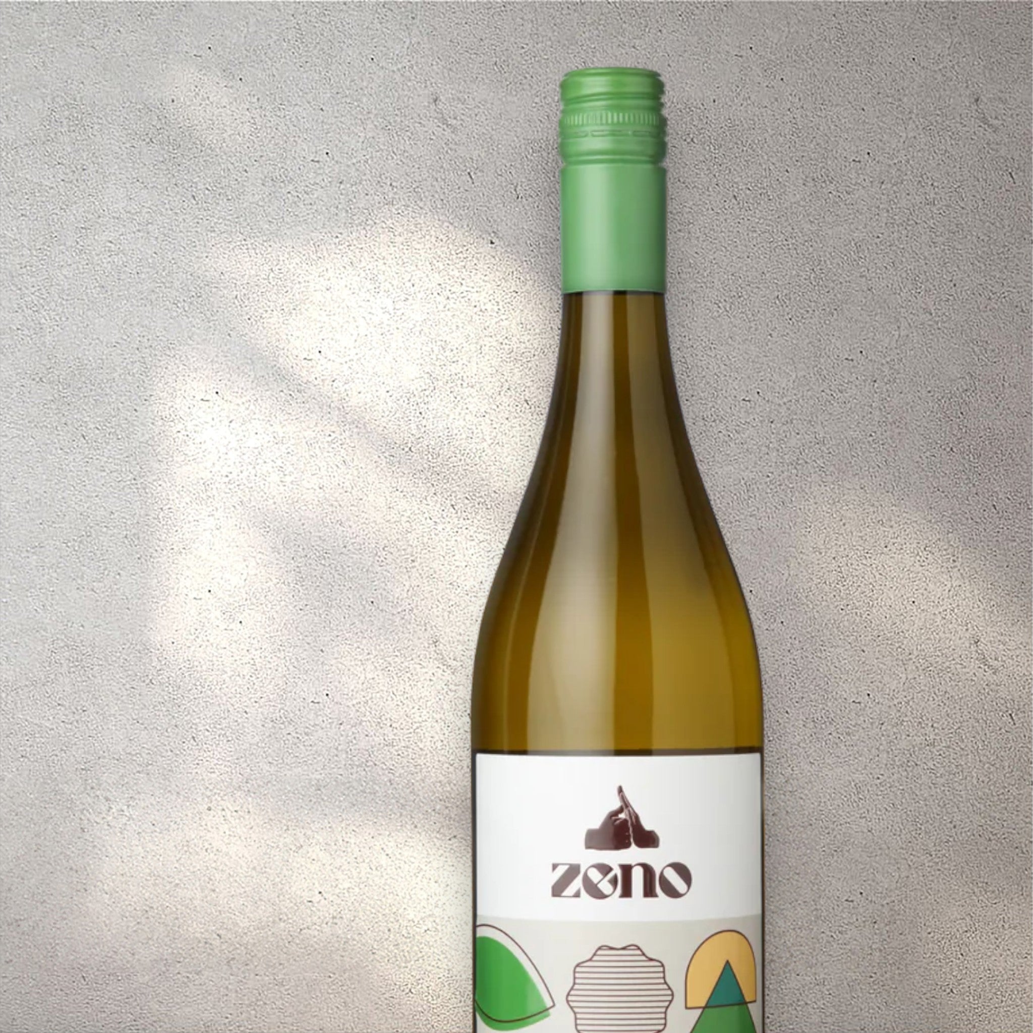Closeup of a Zeno Macabeo alcohol-free white wine bottle with a detailed label, set against a textured concrete wall, highlighting its refined design and pale yellow color.