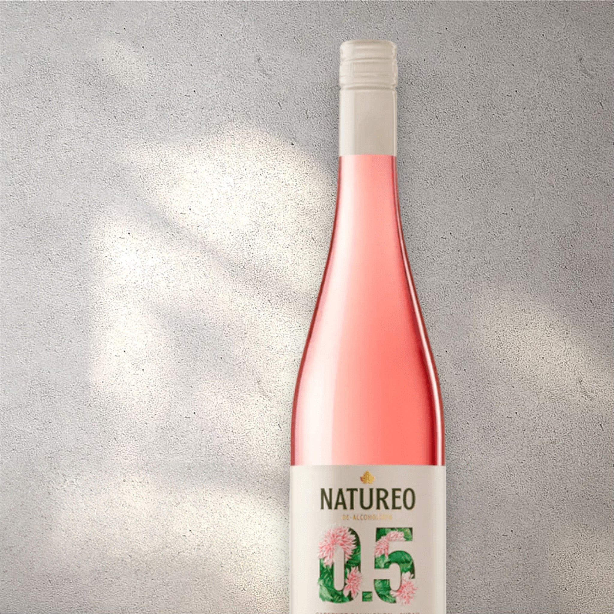 Closeup of a Torres Natureo alcohol-free rosé wine bottle with a detailed label, set against a textured concrete wall, highlighting its refined design and blush pink color.